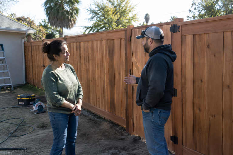 man and woman talking in front of a new fence. 